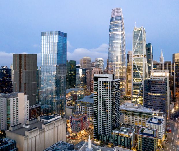 Aerial cityscape view of a dense modern downtown skyline at dusk, featuring numerous high-rise office and residential towers with glass curtain walls, illuminated windows, rooftop structures, and prominent contemporary skyscrapers.
