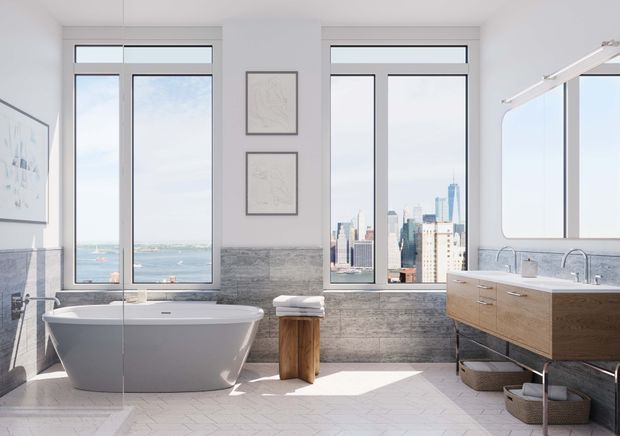 Bright, spacious contemporary bathroom with a freestanding white bathtub, double vanity with timber cabinetry, large black-framed windows, and grey stone-look wall tiling. The room has abundant natural light and city and waterfront views.