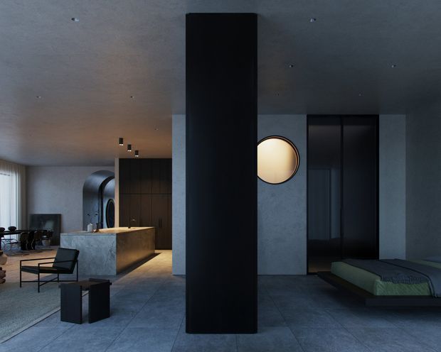 A moody contemporary open-plan interior with a dark central structural or partition wall, a minimalist kitchen with a stone island, a dining area, and a partially visible bedroom zone. The space features concrete-like grey surfaces, dark cabinetry, integrated lighting, a circular wall opening or mirror, and large-format grey flooring. Furniture is sparse and refined, creating a dramatic, gallery-like atmosphere.