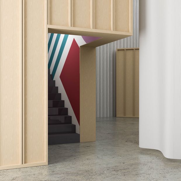 A stylised contemporary interior view showing a dark staircase framed by pale timber built-in joinery and an angular timber opening. A bold geometric mural in teal, white, red and purple appears beside the stairs. The space extends into a concrete-finished open area with vertically ribbed grey wall cladding, a pale timber door, and a curved white partition.