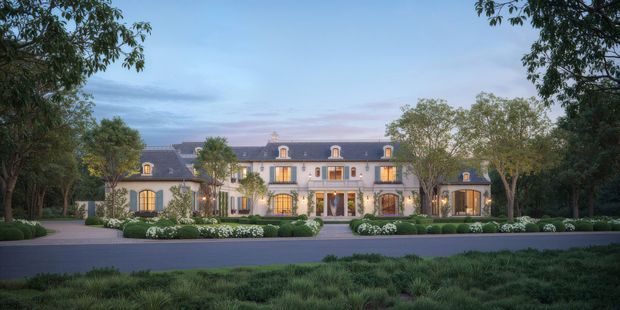 A symmetrical, grand multi-storey mansion viewed from the landscaped front grounds at dusk. The pale facade has tall vertically proportioned windows and French doors, dark slate-like mansard roof sections with dormer windows, small roof projections, and a central entrance. Formal gardens, clipped hedges, ornamental planting, mature trees, and a paved driveway frame the building. The architectural character is classically inspired and refined.