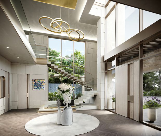 A dramatic, high-end contemporary interior foyer or living space with a sculptural floating staircase, expansive floor-to-ceiling glazing, double-height volume, and a mezzanine or upper-level walkway. Light tiled wall panels contrast with dark timber herringbone flooring and dark structural framing. A large sculptural gold pendant hangs beneath a recessed ceiling feature, while a round pale rug and central floral arrangement anchor the foreground. Lush planting is visible beyond the glazing and around the staircase.