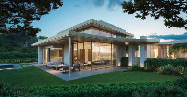 A single-storey contemporary house set within landscaped gardens, shown in a dusk architectural exterior view. The home has a low-pitched, broad overhanging roof, extensive floor-to-ceiling glazing, warm interior lighting, pale rendered or concrete-like walls, and a covered outdoor terrace with lounge furniture. Mature planting and manicured hedges surround the building.