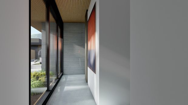 A narrow, minimalist interior corridor or gallery-like passage with a polished grey concrete floor, smooth white walls, and a warm timber slat ceiling. Full-height black-framed glazing runs along one side, overlooking landscaped planting and another building, while a large abstract artwork adds colour to the opposite wall. The space is bright, restrained, and contemporary.