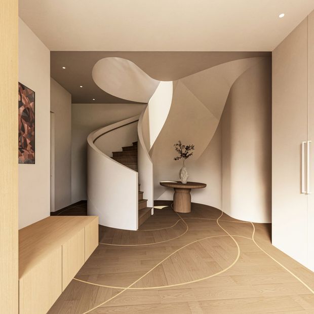 A sculptural residential entry hall with a sweeping curved staircase, flowing organic wall and ceiling forms, light wood flooring with curved inlay details, and built-in pale wood cabinetry. A small round console table and artwork add restrained decorative elements, while concealed and recessed lighting create a warm, refined atmosphere.