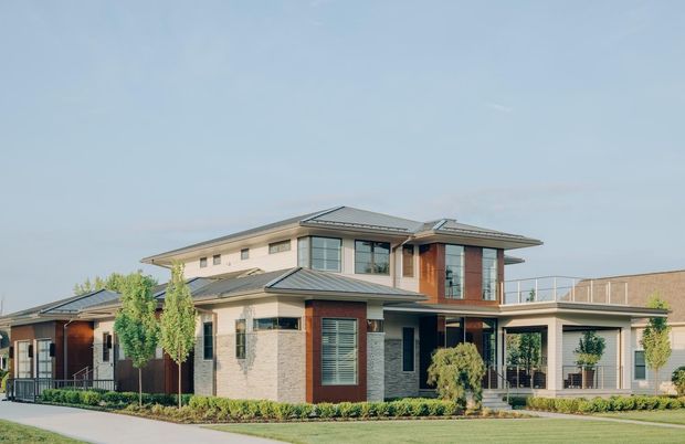 Exterior view of a large, multi-level contemporary residence with layered low-pitched hipped roofs, broad eaves, light masonry walls, dark timber or metal accents, extensive glazing, and landscaped front gardens.