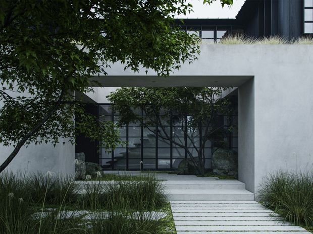 A minimalist contemporary residence viewed from the landscaped front approach. A pale rendered concrete facade forms a deep rectangular portal around full-height black-framed glazing, with broad pale steps and a linear paved walkway leading to the entrance. Dark upper cladding, ornamental grasses, mature trees, and large natural rocks create a restrained modern courtyard-like arrival sequence.
