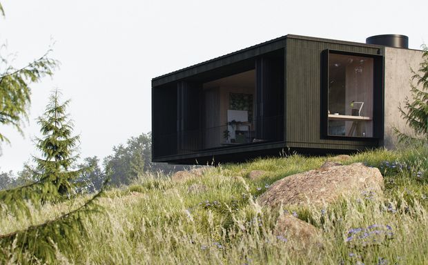 A compact dark-clad modern house or pavilion sits on a rocky, sloping grass-covered site. The rectangular single-storey form has a projecting enclosed volume, deep recessed glazing, a large picture window, and a low-pitched roof. Sparse interior furnishings are visible through the openings, while mature trees and natural grasses surround the building.