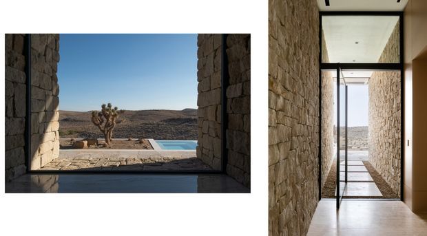 Architectural interior view of a narrow stone-lined passage with full-height black-framed glazing and a reflective dark floor, opening toward a rugged desert landscape and rectangular pool. A second view shows the landscape framed through a deep stone window reveal, emphasizing the connection between the building and arid setting. The architecture is minimal and contemporary, with exposed masonry walls, crisp white ceilings, and strong geometric framing.