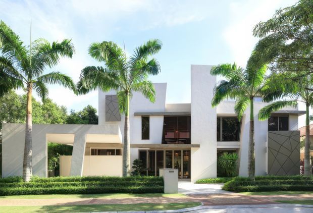 Front exterior view of a large contemporary white residence, featuring strong geometric volumes, flat rooflines, tall recessed glazing, metal entry panels, and a landscaped frontage with palms and clipped hedges.