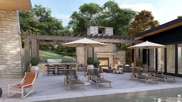 A high-end outdoor entertaining terrace beside a swimming pool, featuring a large paved patio with lounge chairs, dining furniture, umbrellas, and potted plants. A timber pergola with exposed slatted rafters spans the space, connecting stone-clad structures and a dark contemporary pavilion with expansive glazing. A stone outdoor fireplace is visible at the rear, with landscaped greenery beyond.