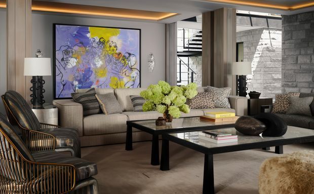 A sophisticated contemporary living room with a large sectional sofa, sculptural lounge chairs, two black-framed coffee tables, layered neutral furnishings, and a large colourful abstract artwork. Warm recessed ceiling lighting, timber-toned wall panels, dark stone surfaces, and a glimpse of a spiral stair contribute to the refined, high-contrast interior.