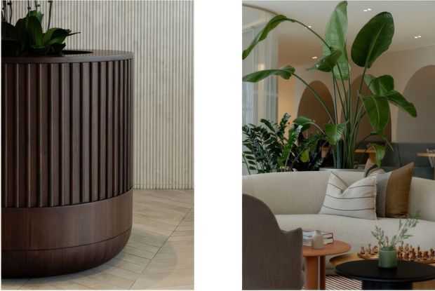 Diptych-style interior image showing a sculptural dark timber fluted planter or built-in cylindrical feature beside a pale vertically ribbed wall and light tiled floor, alongside a warm contemporary living room with curved cream seating, layered cushions, round timber and black coffee tables, abundant indoor plants, and softly arched architectural openings.