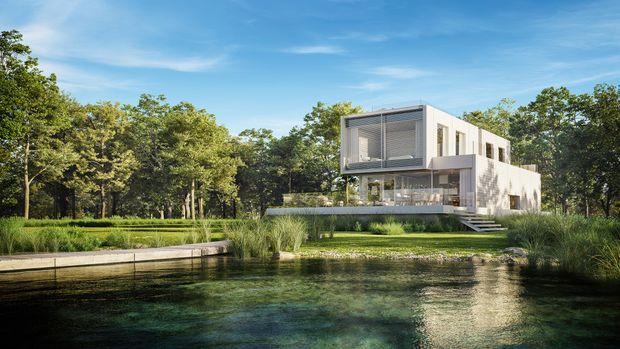 Contemporary two-storey white house set within a wooded landscape beside a reflective pond or natural swimming pool. The residence features a crisp rectilinear form, extensive glazing, a prominent projecting upper-level volume with horizontal screening, broad terraces, and wide steps descending toward the water. Lush grasses and mature trees surround the building, creating a tranquil, nature-integrated setting.