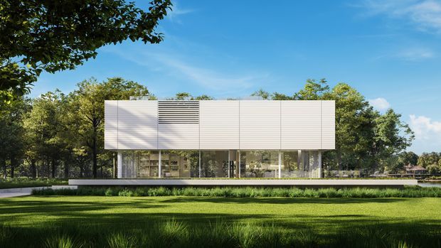 A modern, low-profile rectangular building set within a landscaped green site. The upper facade is clad in pale horizontal panels with a dark louvred ventilation feature, while the transparent ground level has extensive floor-to-ceiling glazing and slender structural supports. A broad terrace or platform extends around the building, with mature trees and lawn surrounding it.