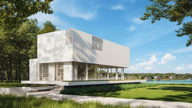 A minimalist modern two-storey waterfront house with a crisp white rectilinear form, horizontal slatted cladding and louvred openings. The upper volume projects over a glazed ground level supported by slender columns, with a low white terrace and stepped entry path surrounded by lawn and mature trees. A calm waterway and neighbouring shoreline are visible beyond.