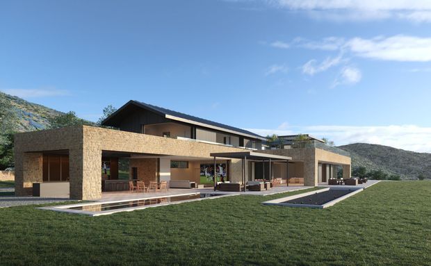 A contemporary multi-level residence set against a mountainous landscape. The building features a long, low horizontal composition, broad flat-roofed volumes, a dark pitched roof over the upper level, extensive glazing, stone-clad walls, covered outdoor terraces, and a narrow reflecting pool or water feature along the lawn.