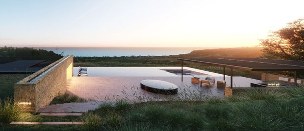 A low-profile modern coastal residence viewed from landscaped grounds, featuring broad flat roof planes, expansive outdoor terraces, a long reflecting or swimming pool, and a sheltered lounge area. A textured stone wall anchors the left side, while the property looks toward a calm ocean horizon and headland at sunset. Native grasses and restrained landscaping soften the architecture.