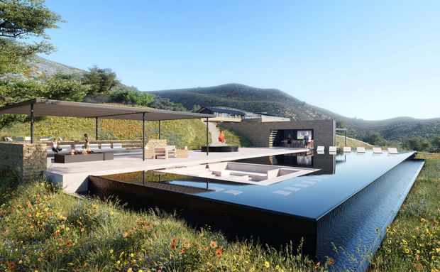 A contemporary flat-roofed hillside residence arranged around a large reflecting pool. The dark geometric building has extensive glazing, broad terraces, a covered outdoor entertaining area, and stepped platforms integrated into a natural mountain landscape with wild grasses and flowering vegetation.