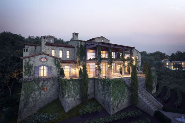 A grand multi-storey stone villa or mansion viewed from the exterior at dusk. The building features warm illuminated windows, red clay tiled roofs, arched openings, tall cypress-like landscaping, extensive climbing ivy, terraces, chimneys, and a long exterior stairway descending through landscaped grounds. The architecture has a strongly Mediterranean and traditional character, with a dramatic elevated setting and formal garden composition.