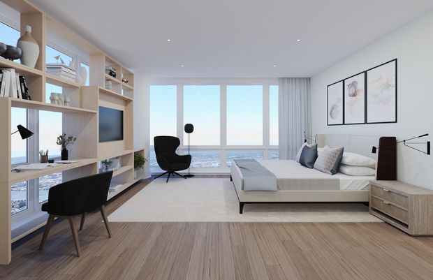 Bright contemporary bedroom with expansive floor-to-ceiling glazing overlooking a coastal or waterfront scene. The room features a low upholstered bed, light timber flooring, a built-in timber shelving and desk wall with television, minimalist bedside furniture, a black lounge chair, soft neutral textiles, and restrained framed artwork. The clean-lined fit-out and pale palette create an airy, refined atmosphere.