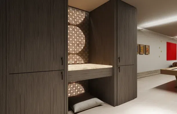 A contemporary interior featuring a tall, dark wood-grain built-in joinery installation with full-height cupboard doors, an inset bench or shelf, and a decorative geometric patterned screen behind it. The space extends into a bright open room with pale flooring, white walls, framed artwork, and a bold red wall panel.