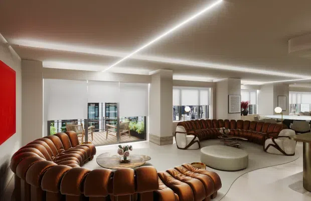 A spacious, high-end contemporary lounge or lobby with curved cognac-brown tufted leather sectional seating arranged around low round coffee tables and ottomans. The room has pale smooth flooring, white structural columns and walls, extensive glazing, linear recessed LED lighting, abstract red wall art, and a polished hospitality-style layout.