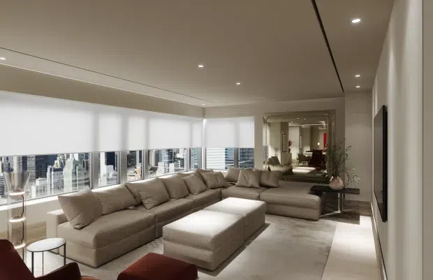 A refined, contemporary living room in a high-rise apartment, featuring a large taupe sectional sofa with matching ottoman, expansive floor-to-ceiling city-facing glazing with roller blinds, a wall-mounted television, recessed ceiling lighting, and a large mirrored opening reflecting the room. The palette is neutral and warm, with streamlined built-in detailing and polished finishes.