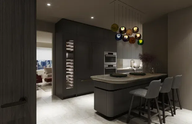A sophisticated, dark-toned contemporary kitchen with a large island and integrated breakfast bar. The kitchen features matte charcoal cabinetry, a pale stone-look benchtop, integrated appliances, a wine rack, and a sculptural cluster pendant light above the island. Four upholstered bar stools line the island, while a living area is visible through the doorway beyond.