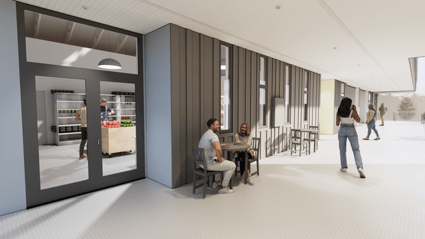A bright contemporary commercial-style interior corridor or covered public walkway. The space features a long glazed and vertically slatted wall, pale tiled flooring, a suspended grid ceiling, café-style tables and chairs, and a dark-framed glazed doorway revealing a refrigerated retail or food display area. People are seated and walking through the space, with strong daylight entering from the open side.