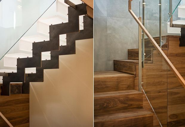 Close-up view of a contemporary interior stairway with dark steel zigzag stringers, warm timber stair treads and adjacent wall cladding, and clear glass balustrades with timber handrails. The composition emphasizes the staircase construction and material contrast.