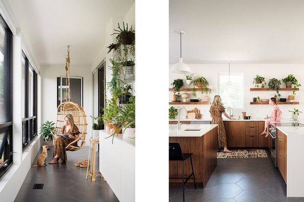 A bright split-view residential interior featuring a plant-filled hallway or sunroom on the left and a contemporary kitchen on the right. The left space has expansive black-framed glazing, dark tiled flooring, a hanging wicker chair, abundant indoor plants, and a seated person with a cat. The kitchen has white walls and cabinetry, warm timber island and lower cabinets, open timber shelves with plants, pendant lighting, and dark hexagonal floor tiles.