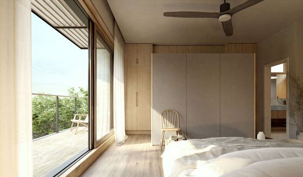 A serene, minimalist bedroom with a low-profile bed in the foreground, pale timber flooring and built-in timber wardrobe cabinetry. Full-height glazed sliding doors open to a timber balcony, bringing in abundant natural light and views of greenery. A ceiling fan, sheer curtains, and a simple timber chair complete the calm, natural interior.
