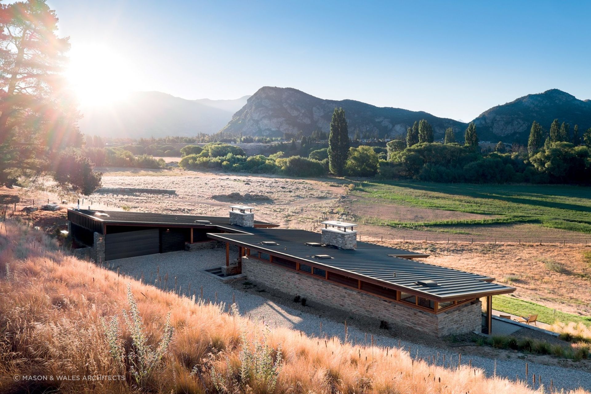 The distinctive sharp, sloping roof and two large schist chimneys of the Cardrona River House by Mason &amp; Wales Architects are great features of this impressive home. | Photography: Dennis Radermacher