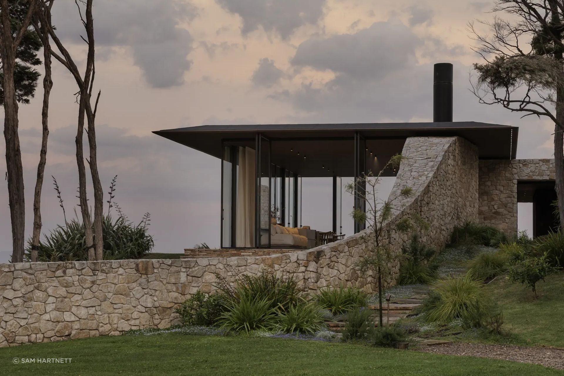 At Waiheke House by Cheshire Architects, Aria limestone from The Natural Stone Co. is used as both structure and landscape gesture, anchoring the home within its coastal setting.
