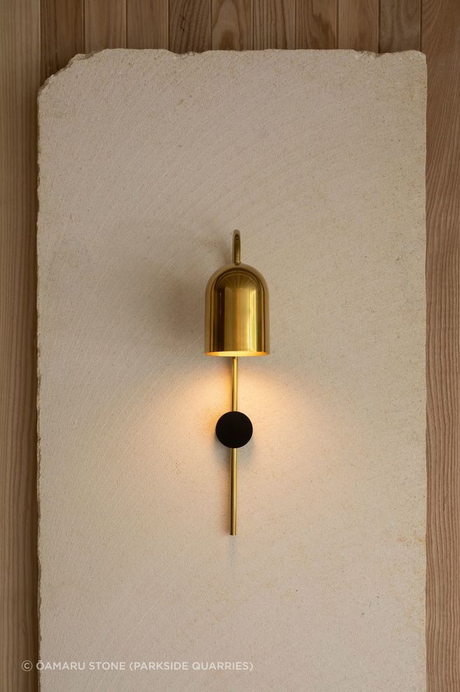 A sleek golden sconce illuminates the natural beauty of the limestone.
