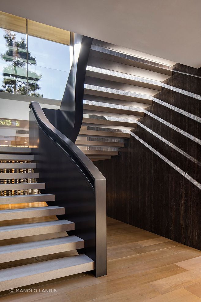 In the stairwell, McClean Design uses overhead glazing to turn circulation into an experience, letting daylight fall through the space and animate the dark timber wall beside it.