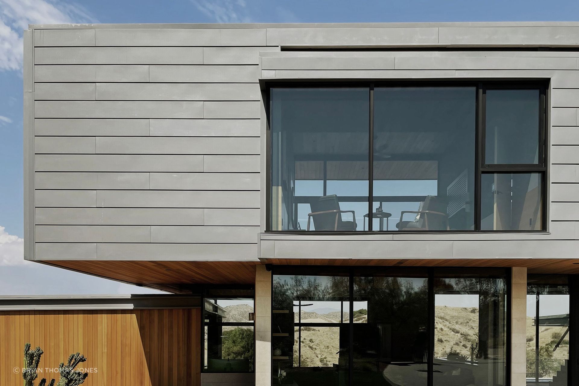 The entry-facing pavilions are clad in zinc, wrapped in a soft C-shape at the roofline and eaves rather than boxed in, paired with fire-rated cedar siding that continues from exterior straight into the interior.