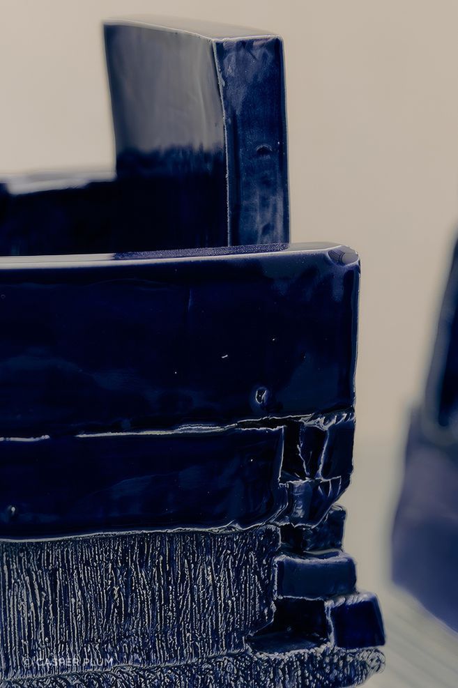 The high-gloss blue glaze gives the works depth and reflection, catching light across their irregular edges, recesses and stacked surfaces.