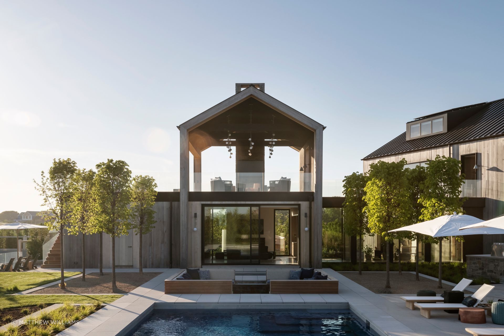 An Escape in the Hamptons resolves its central tension through material choice more than through plan. Alaskan yellow cedar, chosen for the exterior, grays out within months of installation. Limestone and patinated bronze were selected specifically because wear reads as improvement rather than damage.