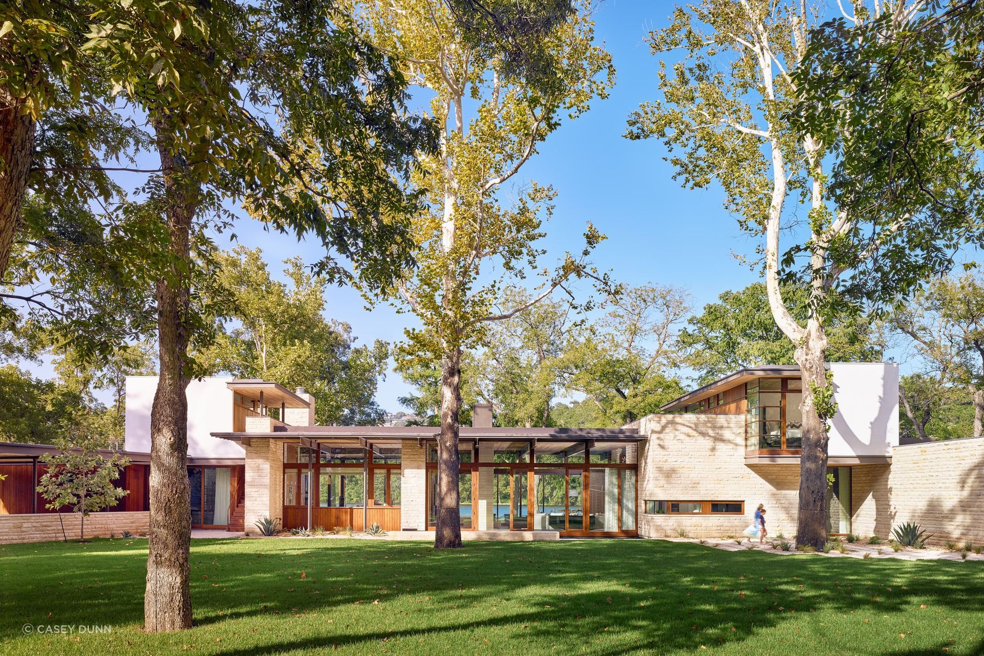 This sinuous lake-front home’s light floating roofs are anchored to its site by heavy rusticated limestone masses, while its horizontal footprint is spread out and sewn through the vertical punctuation of mature sycamore, cypress and pecan trees.