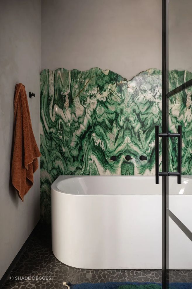 Book-matched slabs of green marble and flooring of sliced river stones form a dynamic backdrop to the primary bath’s Kaldewei tub.