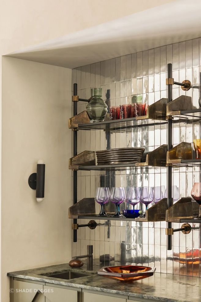 Shelving by Studio Van Den Akker complements the bar’s mirrored tilework and custom cabinetry; sconce by Workstead.