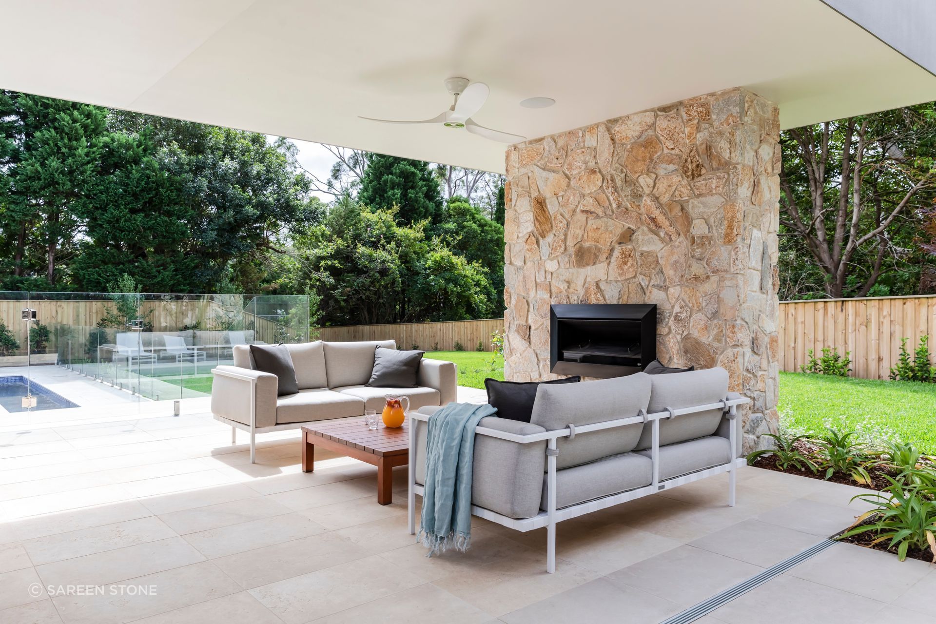 Lavarosa Limestone pavers ground an outdoor living space at Seaforth, anchored by a natural stone feature fireplace and views to the pool beyond.