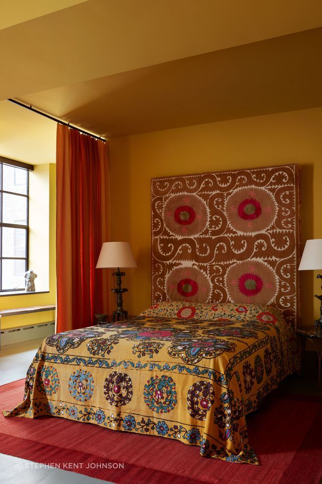 The guest suite is painted in a deep yellow by Ressource Paints; the headboard is upholstered in an antique Suzani; the curtain is a Holland & Sherry linen.
