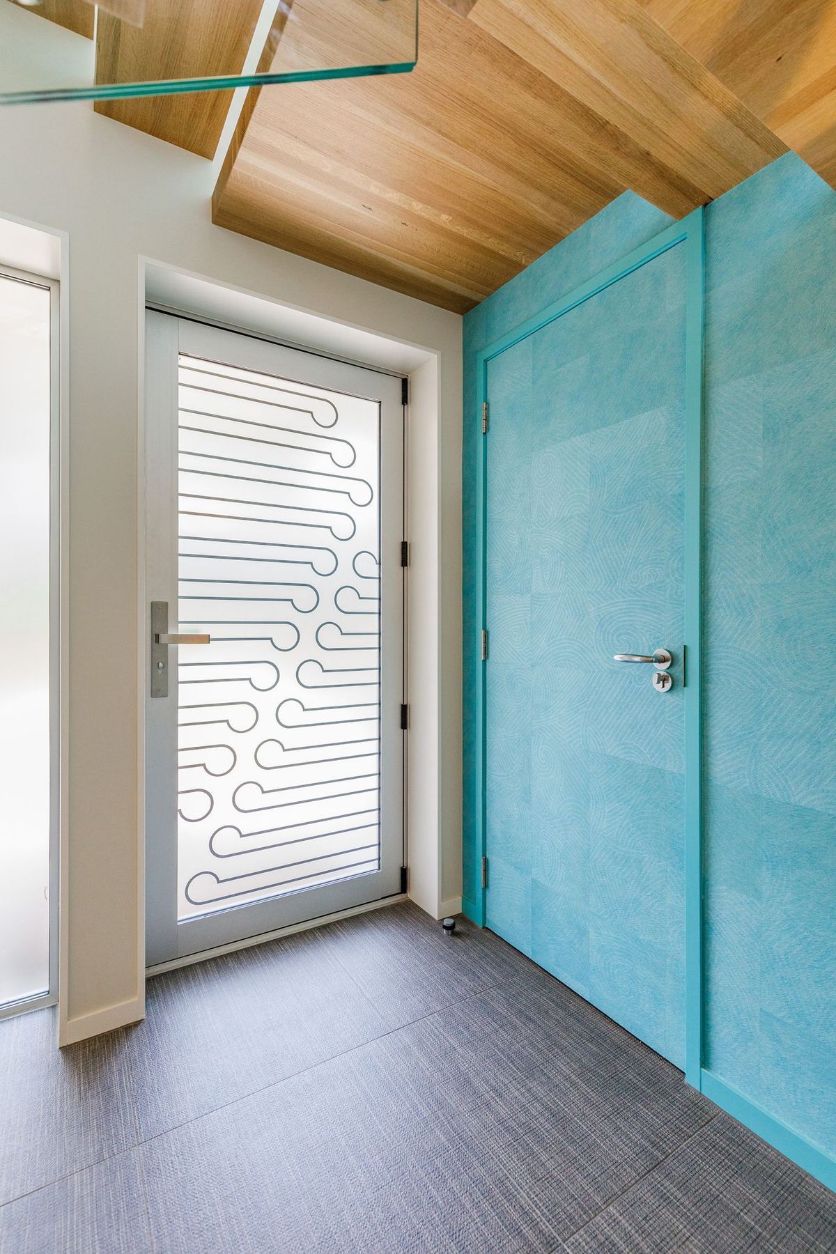 The entrance door really makes an impact. The glass received a customised print using the latest direct-on-glass digital printing technology.  The koru pattern is a welcoming symbol of unfolding.   The feature wallpaper is Elitis Wallpaper Natives Maori. It runs floor to ceiling over two stories and provides the tone for the upstairs areas.