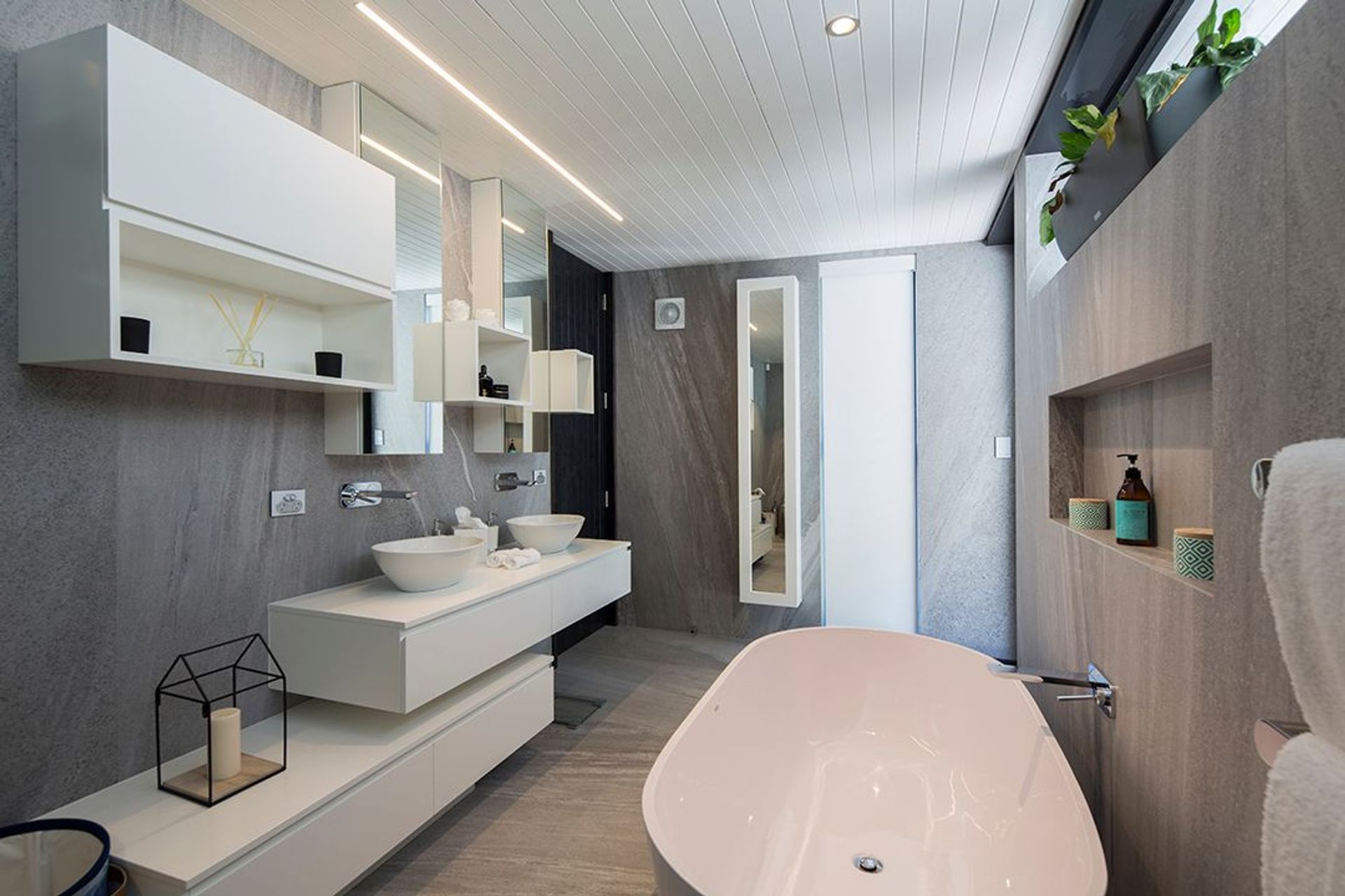 The ensuite bathroom is crisp and clean in grey stone and white. White stone bath, basins, joinery and ceilings reflect a minimalist colour palette.