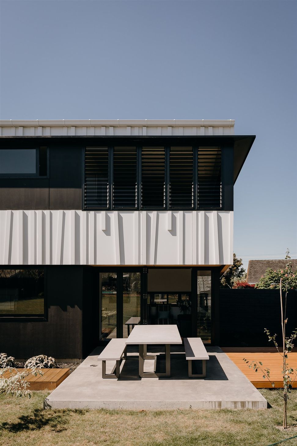 The main living area opens onto the private, rear backyard, whose central space is atop a concrete slab met on either side by timber decking that runs the length of this long, narrow house