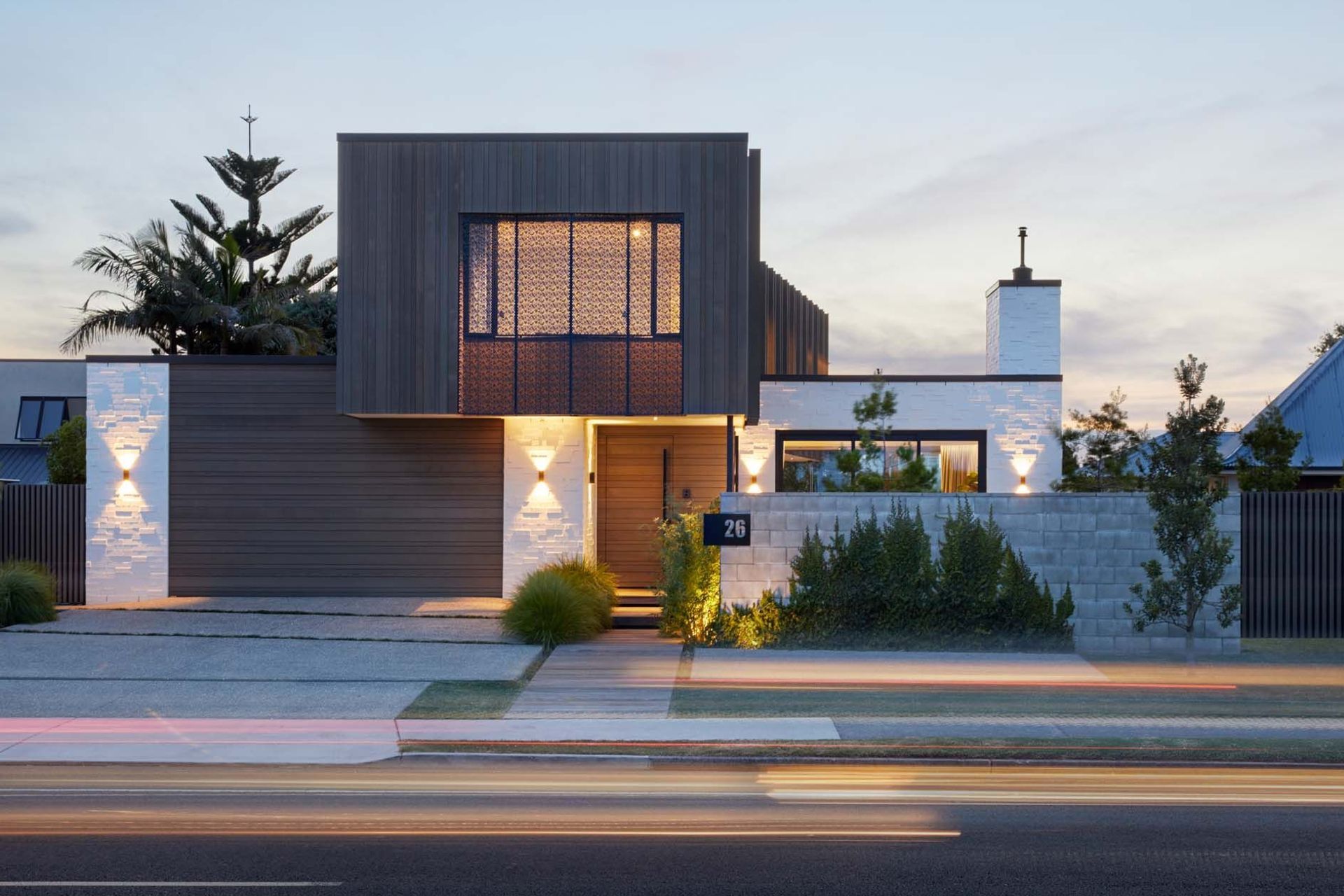 The street elevation seen at dusk shows how the house is beautifully lit to emphasise the textural material qualities of the cladding and the screening.