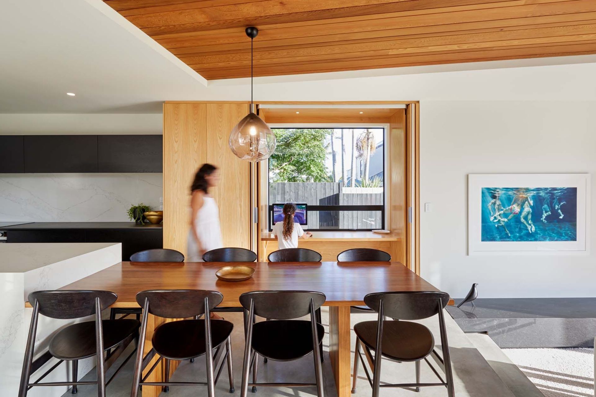 Timber furniture, cabinetry and ceiling adds warmth to the monochromatic colour scheme in the kitchen and dining area.